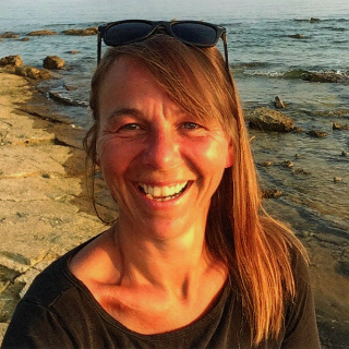 Andrea Schikora von Studio Schikoko lächelt am Meer während einer kreativen Auszeit in der Natur.