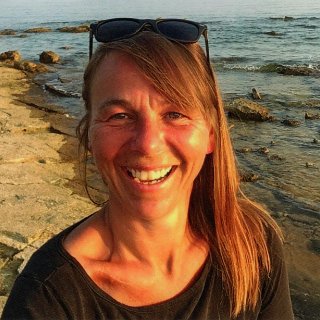 Andrea Schikora von Studio Schikoko lächelt am Meer während einer kreativen Auszeit in der Natur.